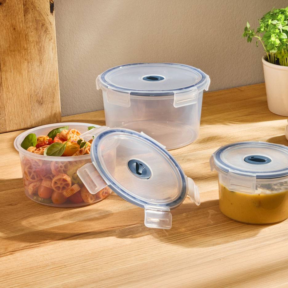 Récipients ronds transparents avec couvercles à bord bleu, l'un rempli de salade de pâtes, l'autre de soupe.