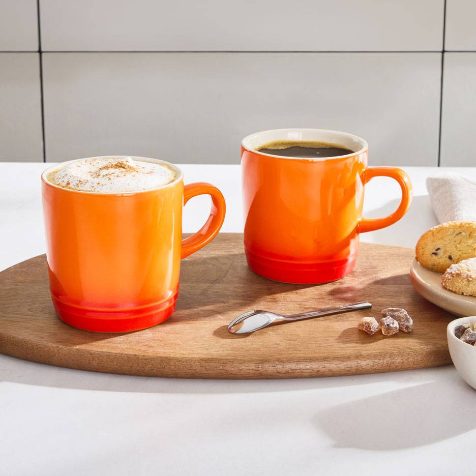 Deux tasses à café orange sur un plateau en bois, l'une avec du café mousseux, l'autre avec du café noir.