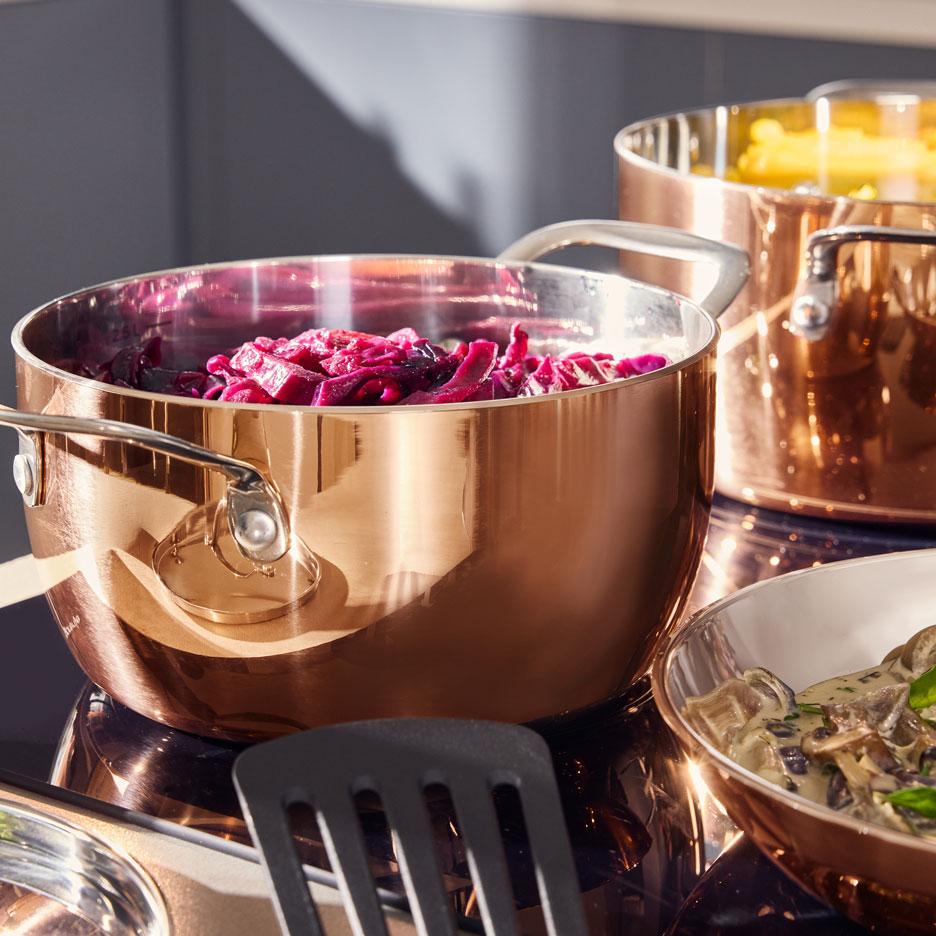 Casseroles en cuivre avec chou rouge et pâtes sur une plaque de cuisson, avec un bol de ragoût de champignons.
