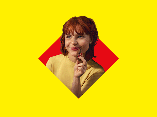 Une femme rousse souriante tenant un chocolat sur un fond jaune et rouge.