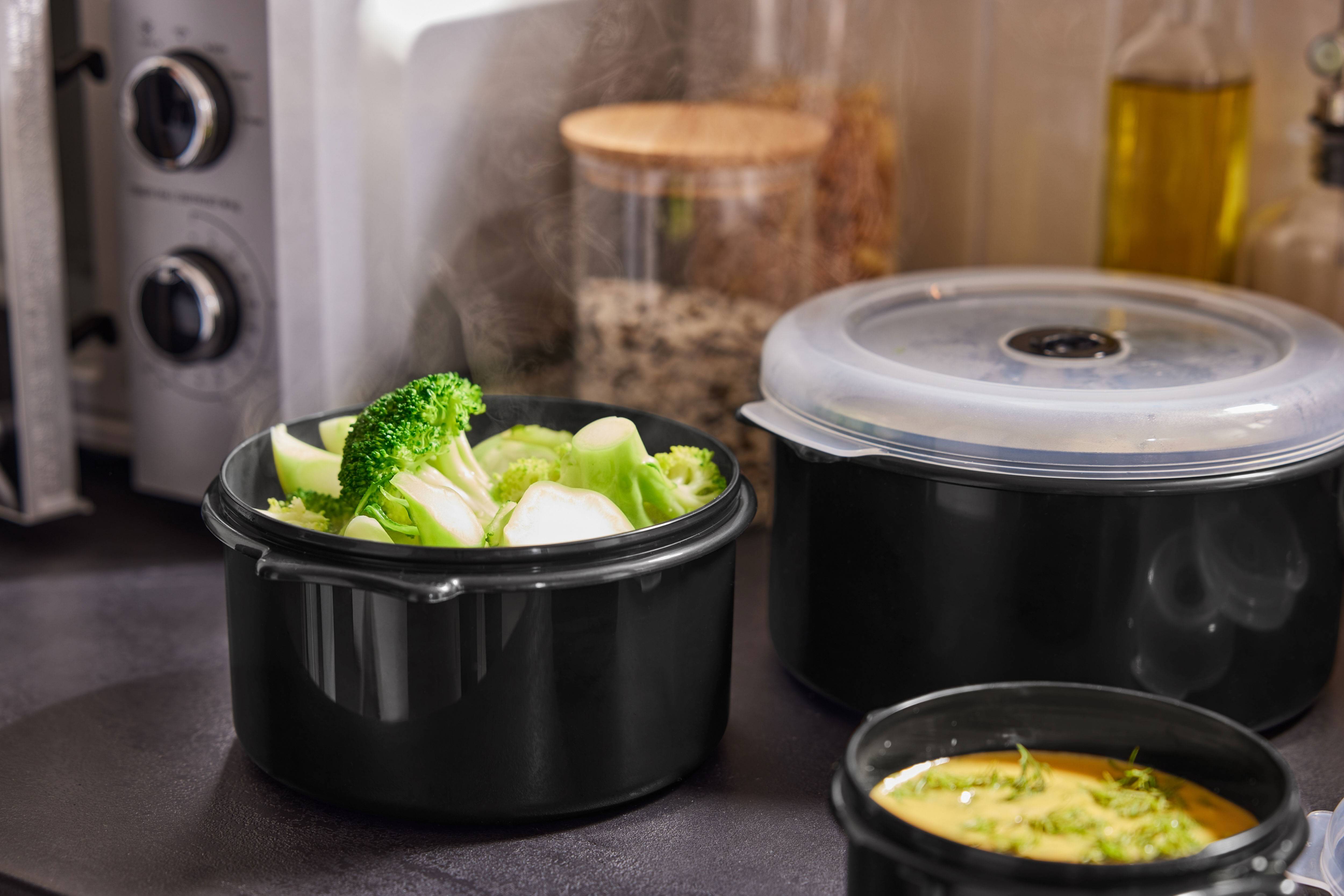 Brocolis fumants et autres plats dans des récipients noirs sur le comptoir de cuisine.