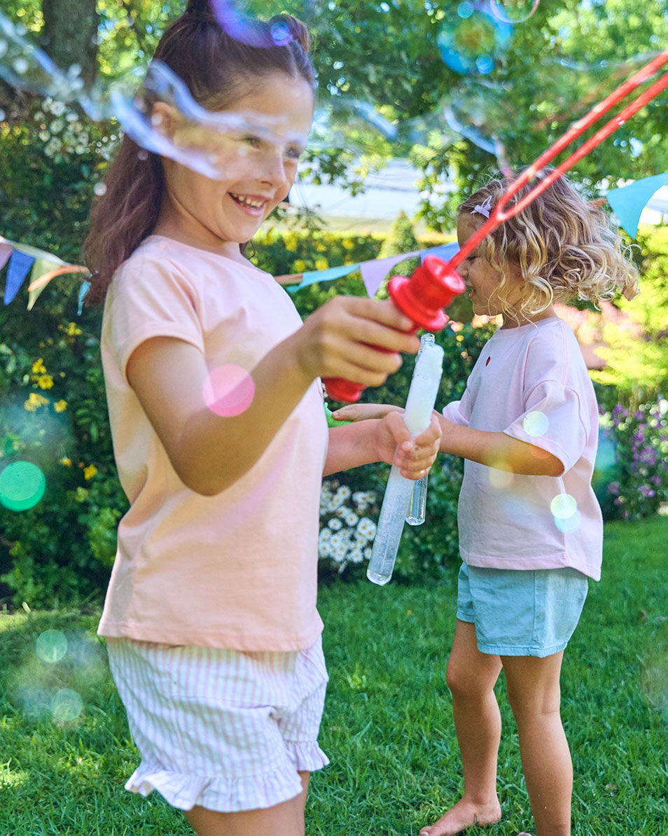 Deux filles jouent avec des bulles dans le jardin, vêtues de vêtements d'été.