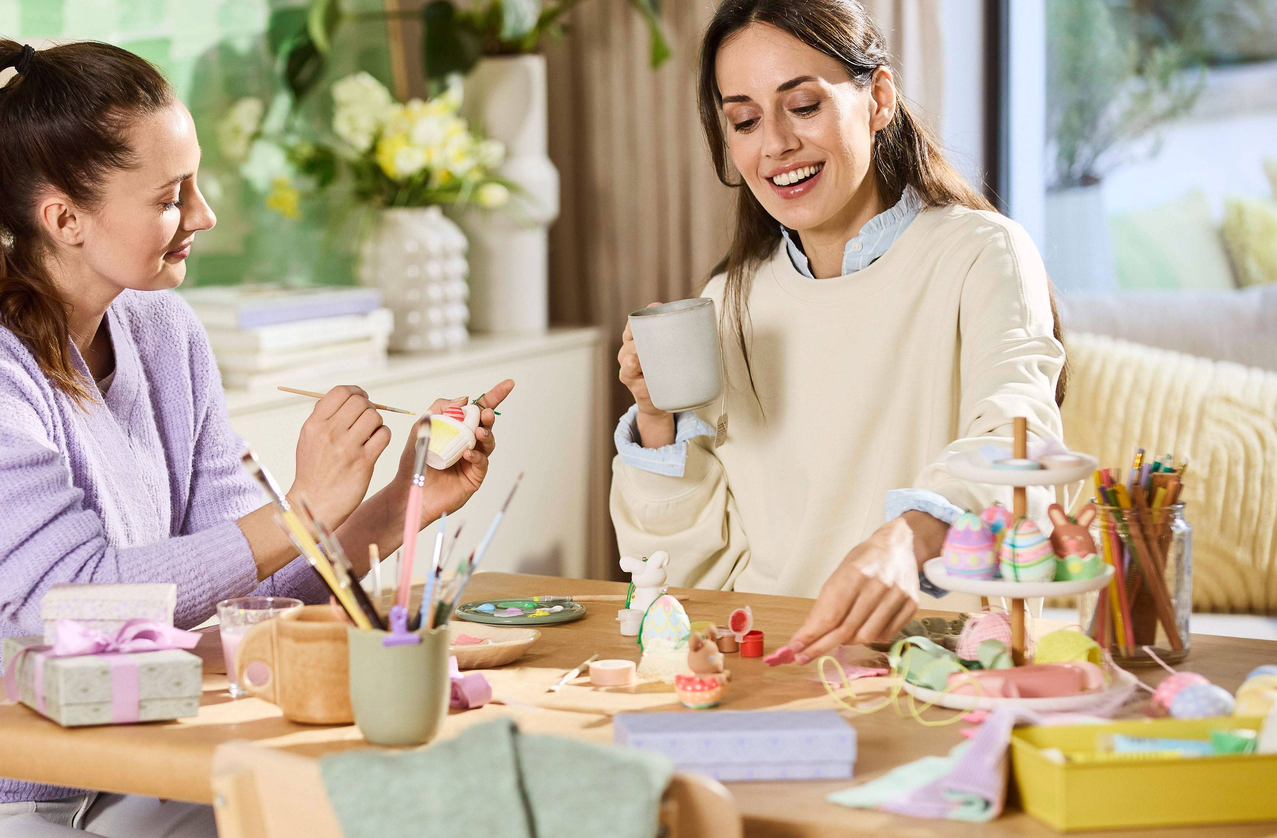 Deux femmes peignent des œufs de Pâques et des décorations, table pleine de fournitures artistiques.