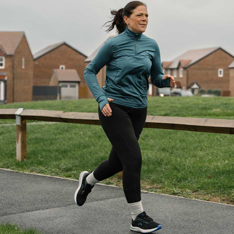 Femme en tenue de sport courant sur un chemin extérieur.