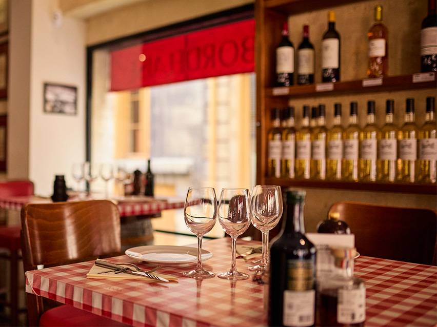 Table de restaurant avec nappe à carreaux rouges et blancs, verres à vin et bouteilles de vin.
