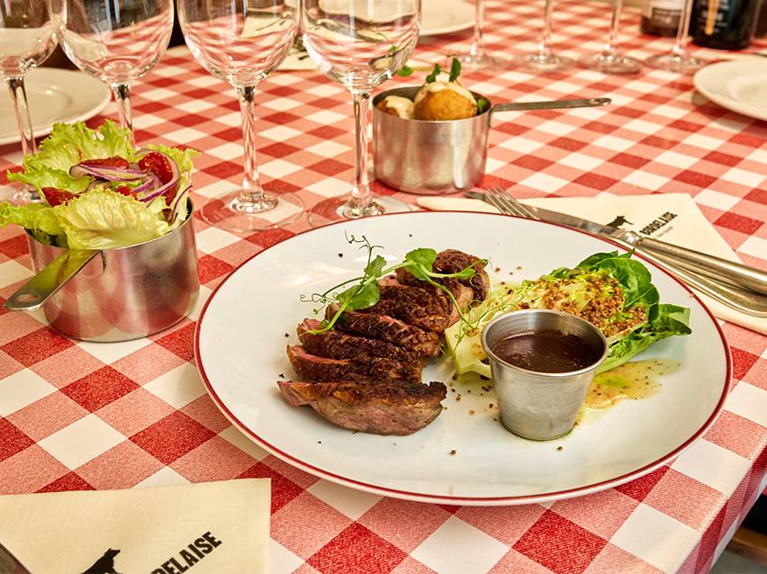 Steak tranché avec salade, sauce et accompagnements sur une nappe à carreaux rouges et blancs.