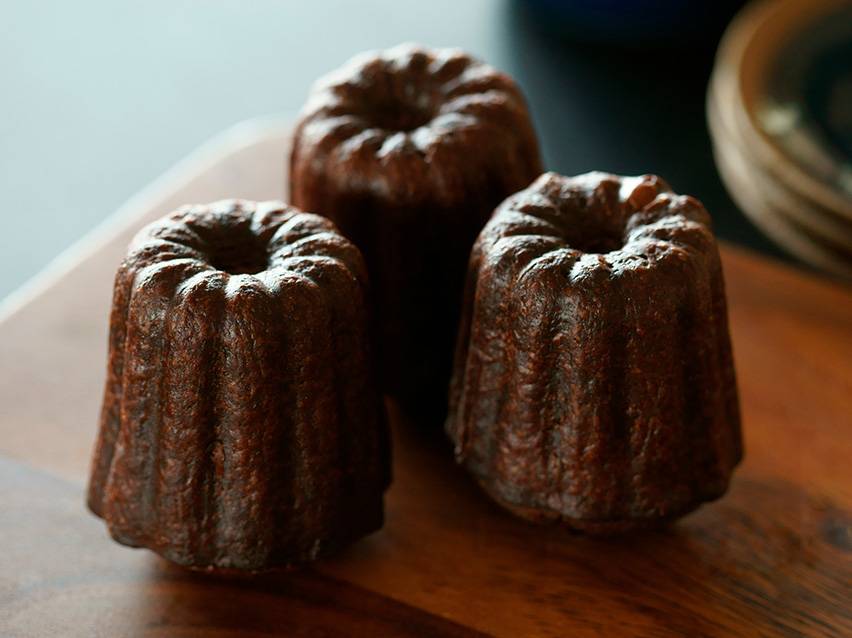 Trois canelés de Bordeaux sur une planche en bois.