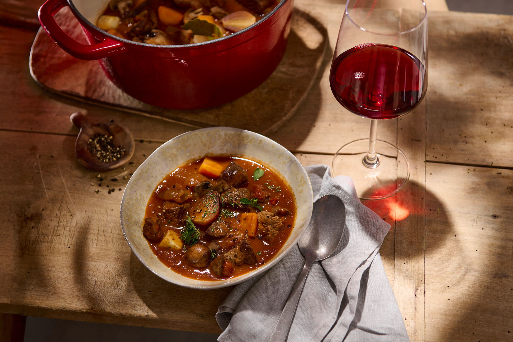 Ragoût de bœuf et légumes dans un plat et un bol, avec un verre de vin rouge.