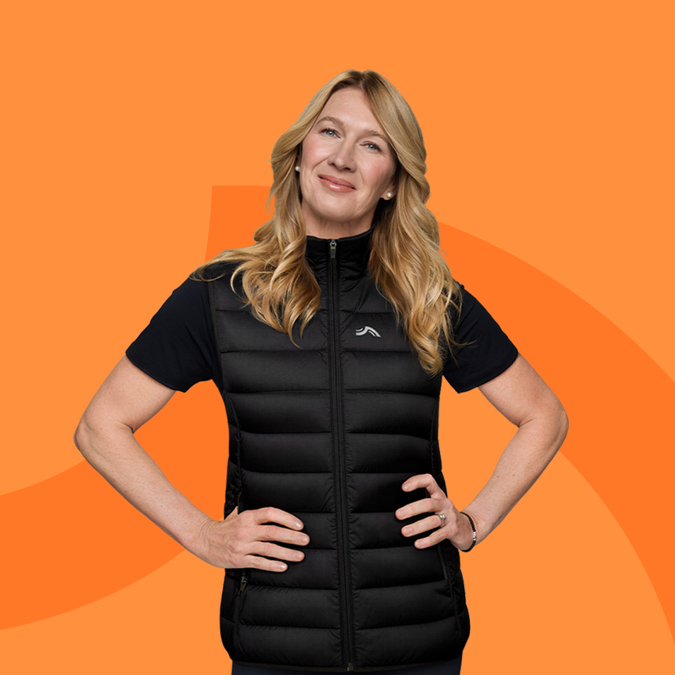 Femme en gilet matelassé noir et t-shirt noir, souriante, sur fond orange.