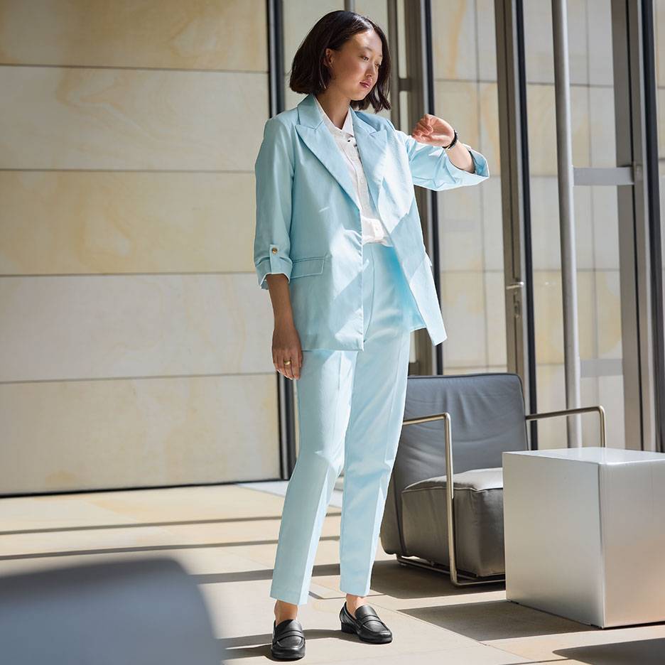 Femme en costume bleu clair avec blazer et pantalon, portant des mocassins noirs.
