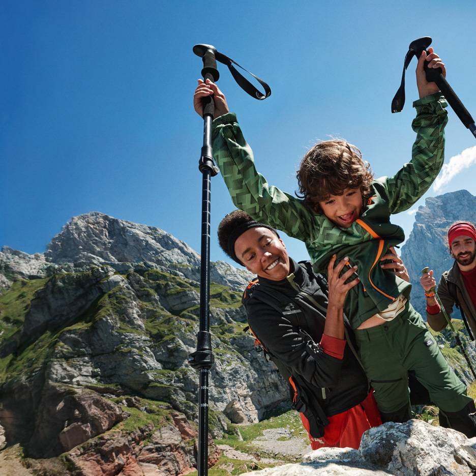 Famille en randonnée avec bâtons de trekking et vêtements d'extérieur en montagne.