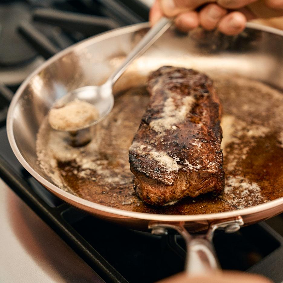 Un steak cuit dans une poêle avec du beurre arrosé dessus.