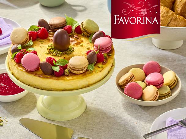 Un cheesecake décoré de macarons, framboises et œufs en chocolat, avec un bol de macarons à côté.