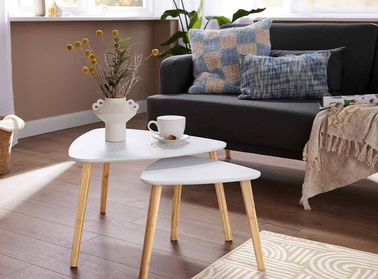 Ensemble de tables gigognes blanches triangulaires avec pieds en bois clair, dans un salon moderne.