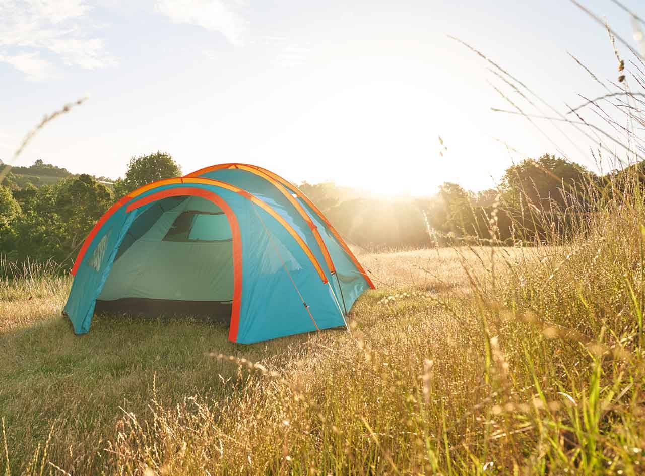 Une tente de camping bleue et orange est installée dans un champ herbeux au lever du soleil.
