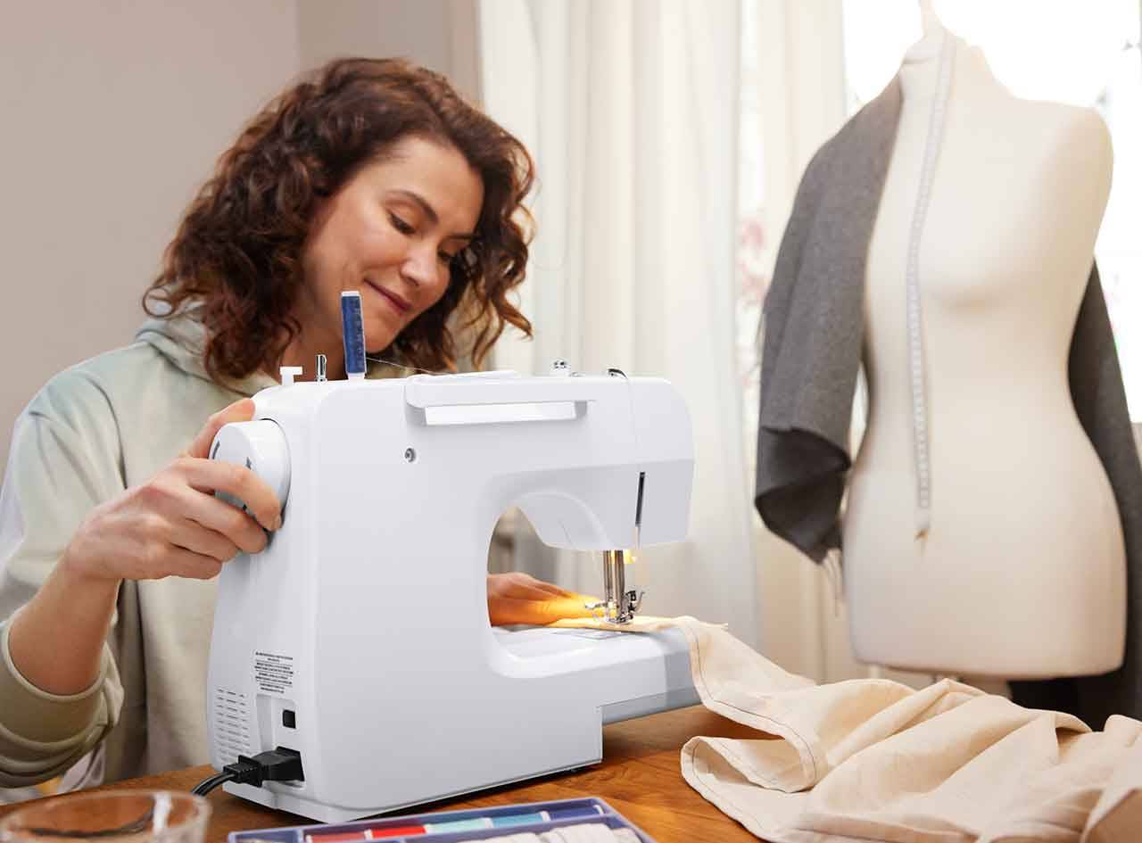 Une femme utilise une machine à coudre blanche pour coudre un tissu beige.