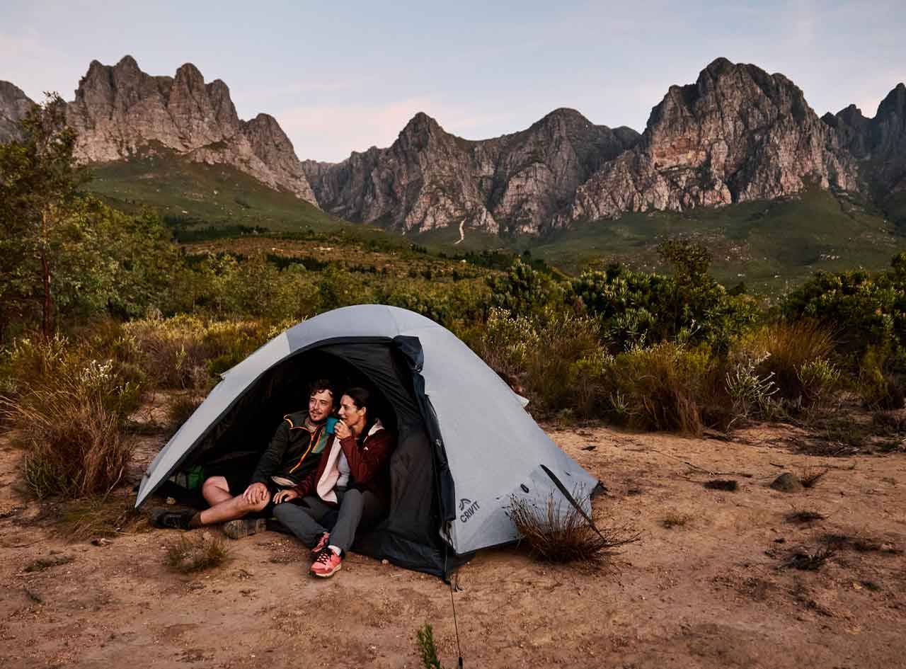 Un couple se relaxe dans une tente Quechua au pied de montagnes majestueuses.