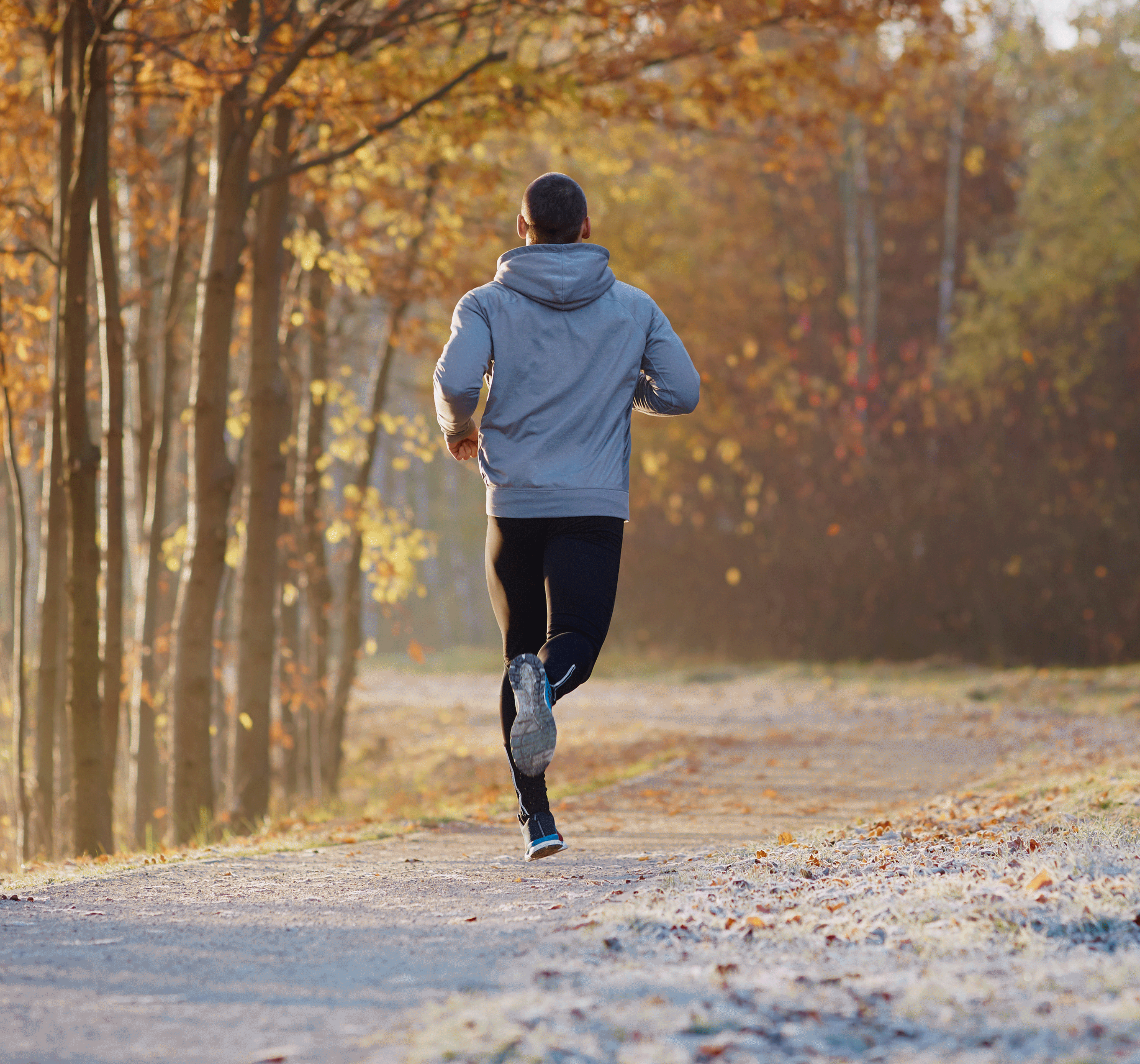 Homme en tenue de sport courant sur un chemin forestier en automne.