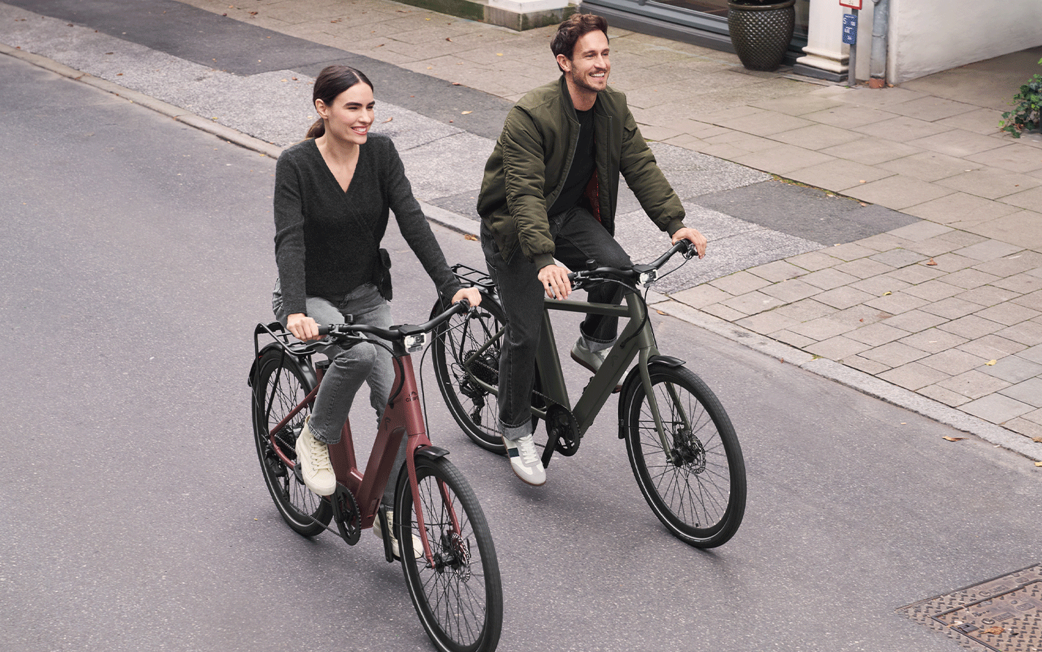 Deux personnes souriantes à vélo sur une route, l'une sur un vélo rouge, l'autre sur un vélo vert.