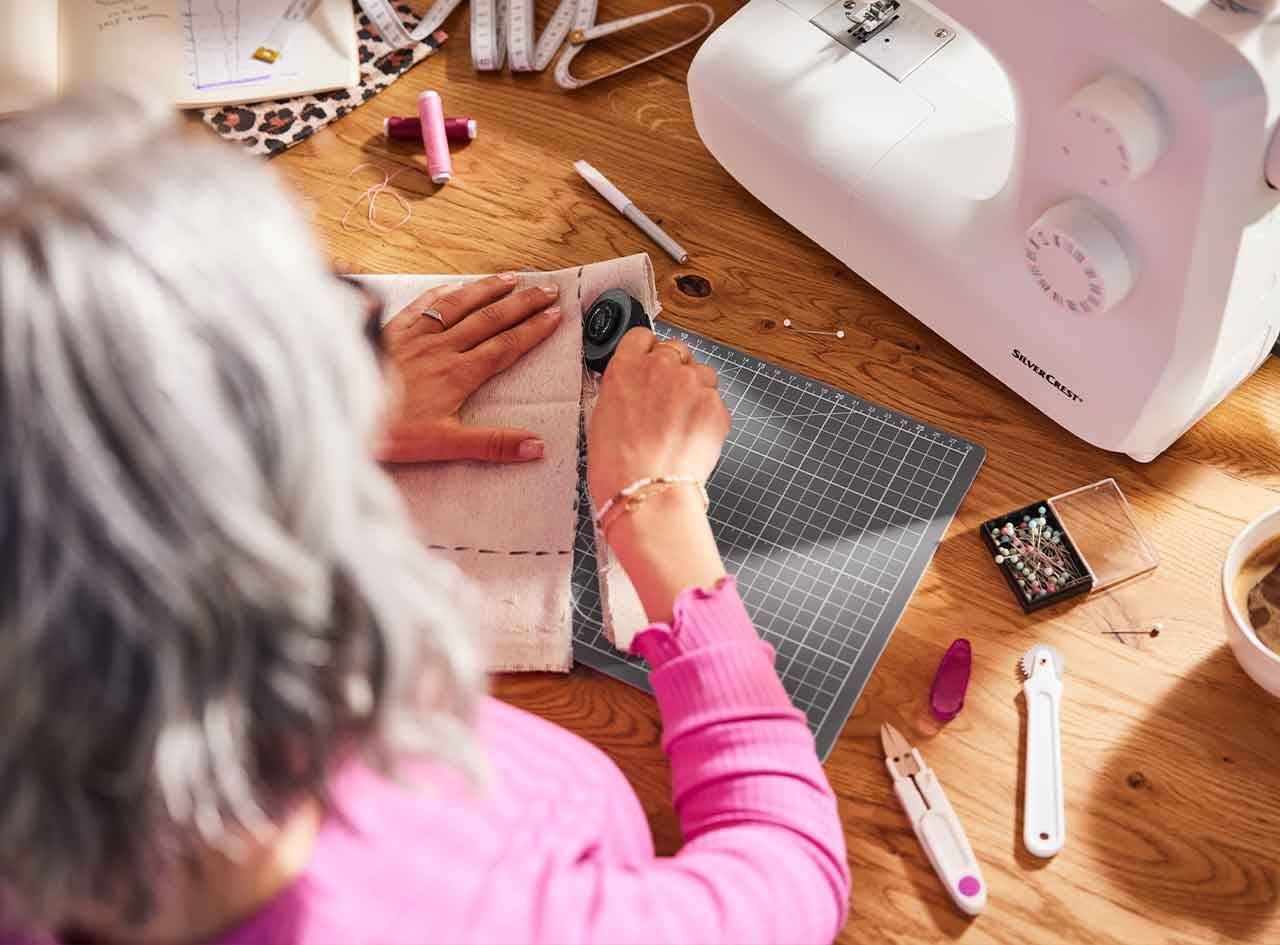 Une femme utilise une machine à coudre Silvercrest et des outils de couture pour travailler sur un projet de couture.