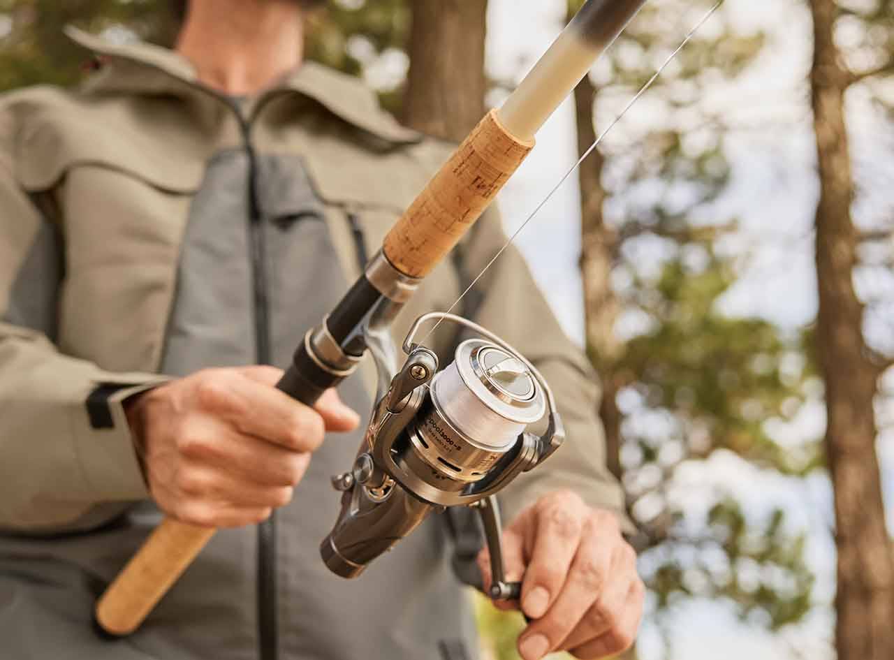 Un homme tient une canne à pêche Daiwa avec un moulinet.