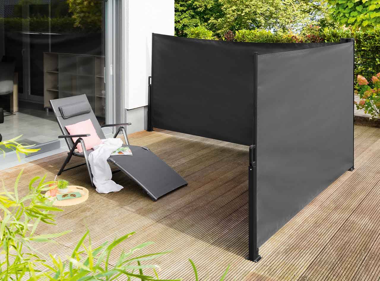 Un écran de jardin gris foncé crée un espace intime sur une terrasse, près d'une chaise longue.