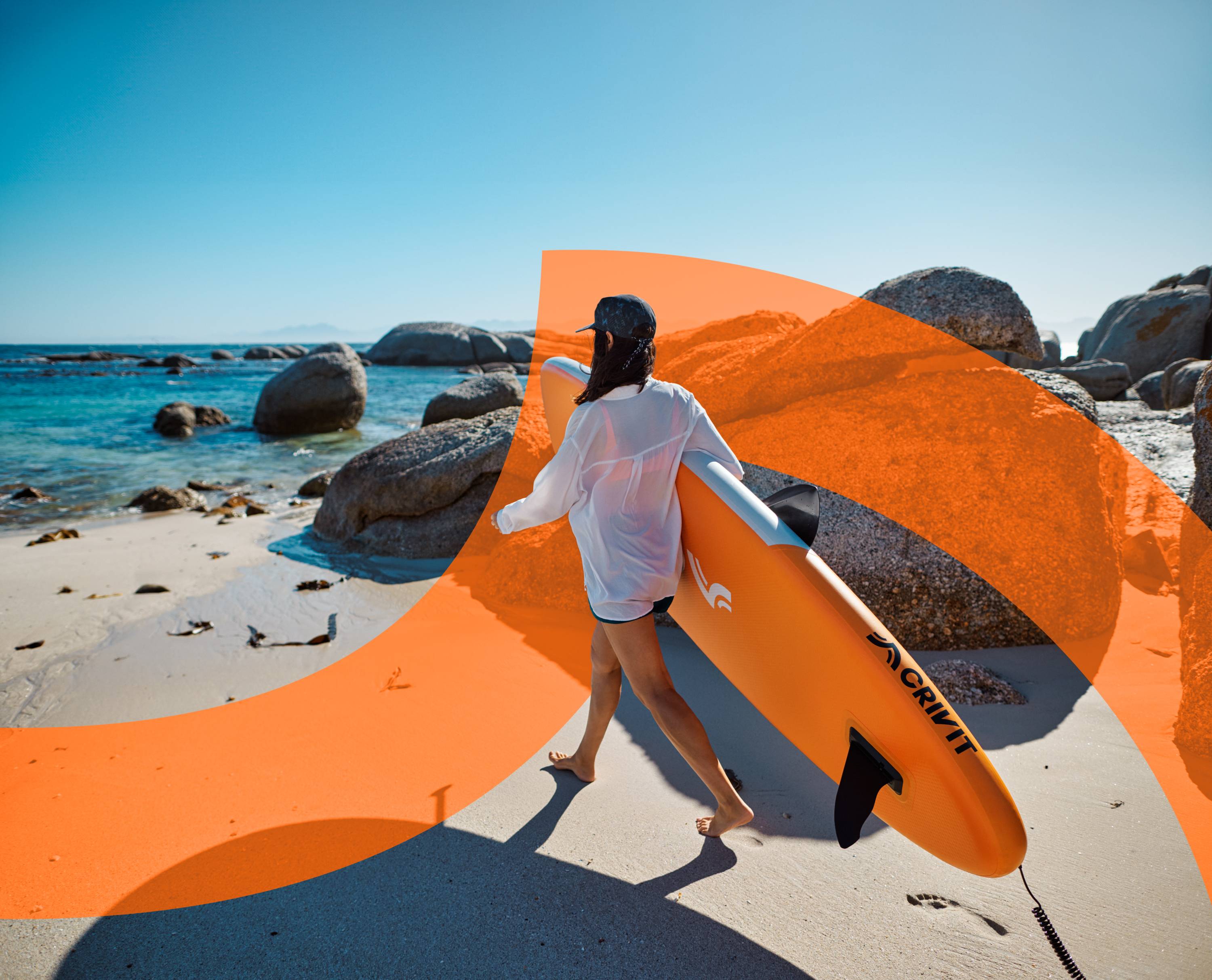 Femme marchant sur une plage de sable avec une planche de stand up paddle orange.