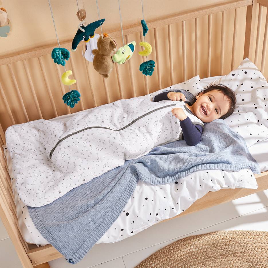 Bébé heureux dans une gigoteuse étoilée dans un lit en bois avec mobile.
