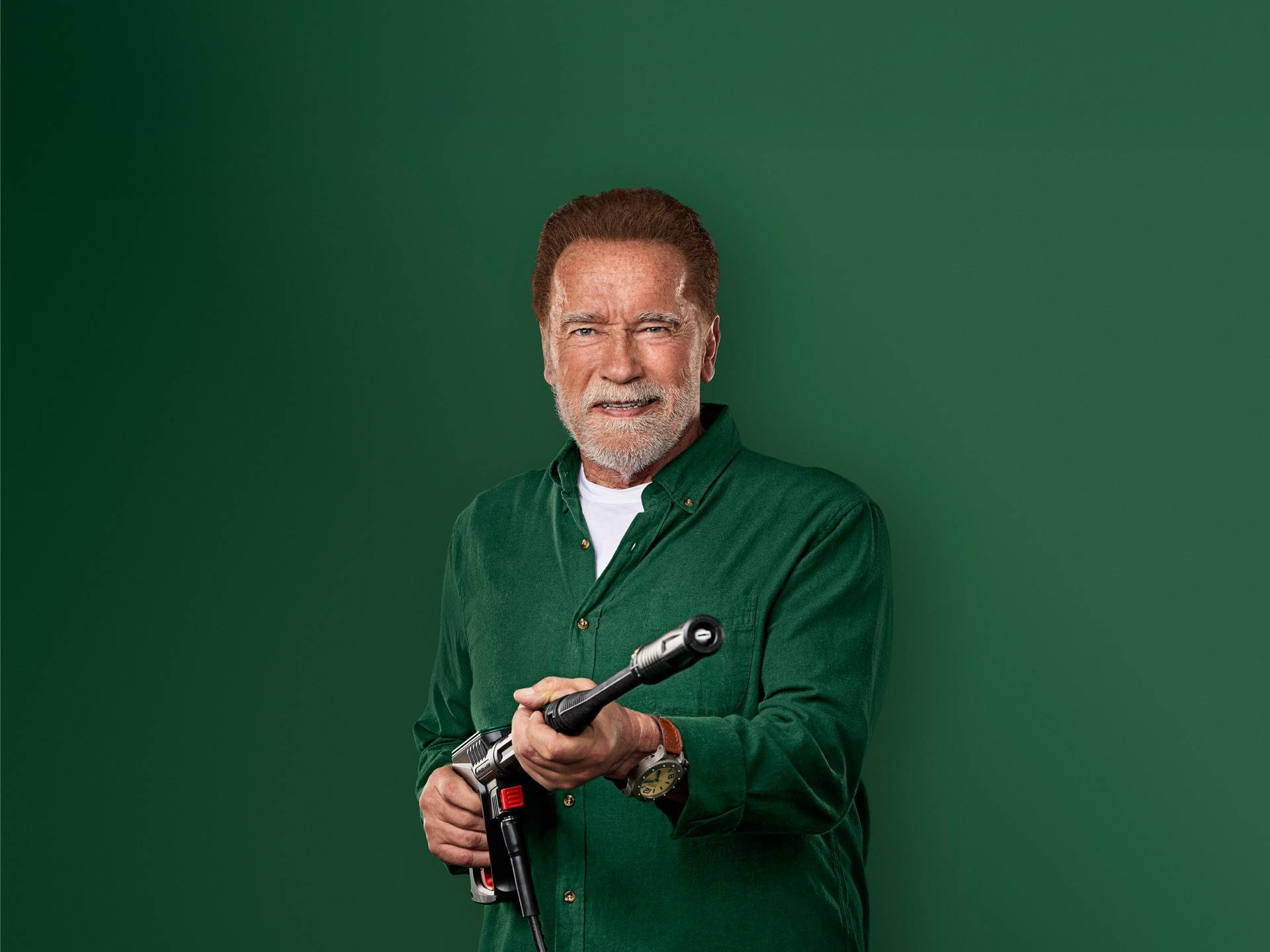 Arnold Schwarzenegger sourit, tenant un pistolet de nettoyeur haute pression.