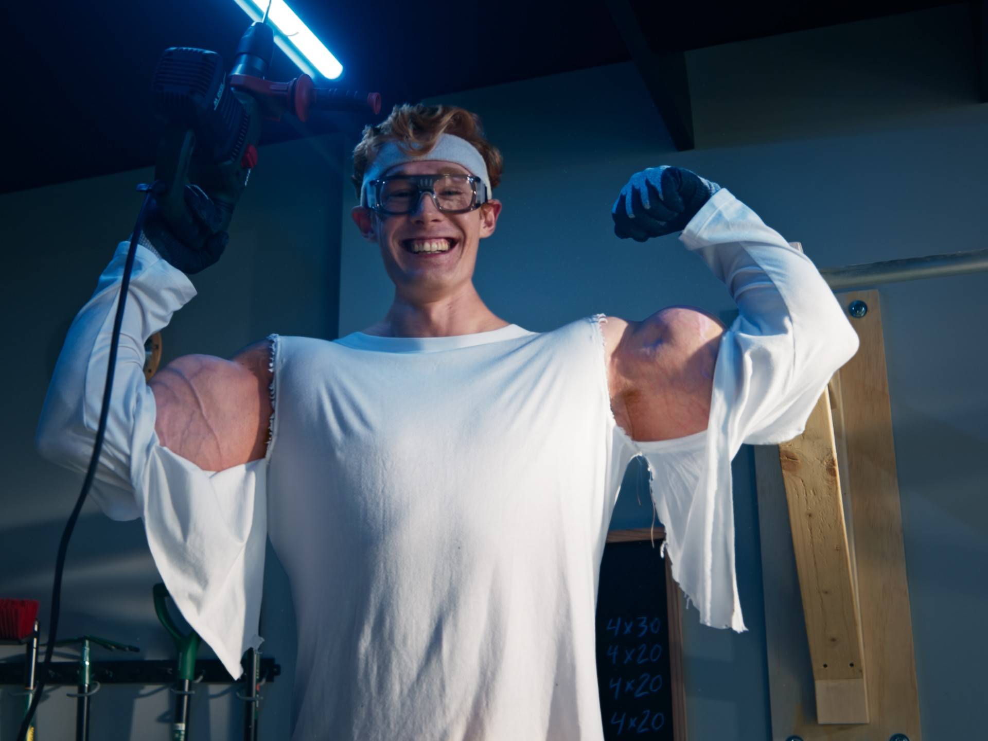 Homme avec des outils et des muscles exagérés souriant dans un atelier.