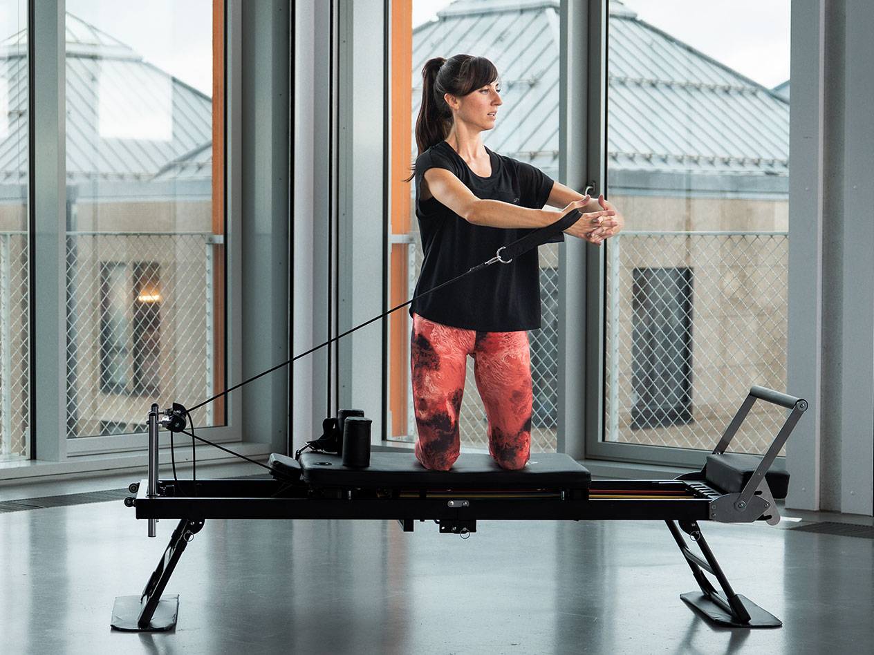 Femme faisant du Pilates sur un reformer noir dans une pièce lumineuse.