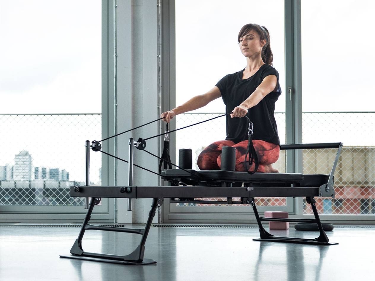 Femme faisant du Pilates sur une machine reformer avec un fond urbain.