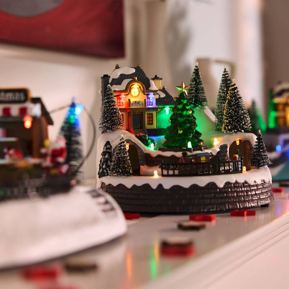 Village de Noël avec gare illuminée, arbres et train miniature.