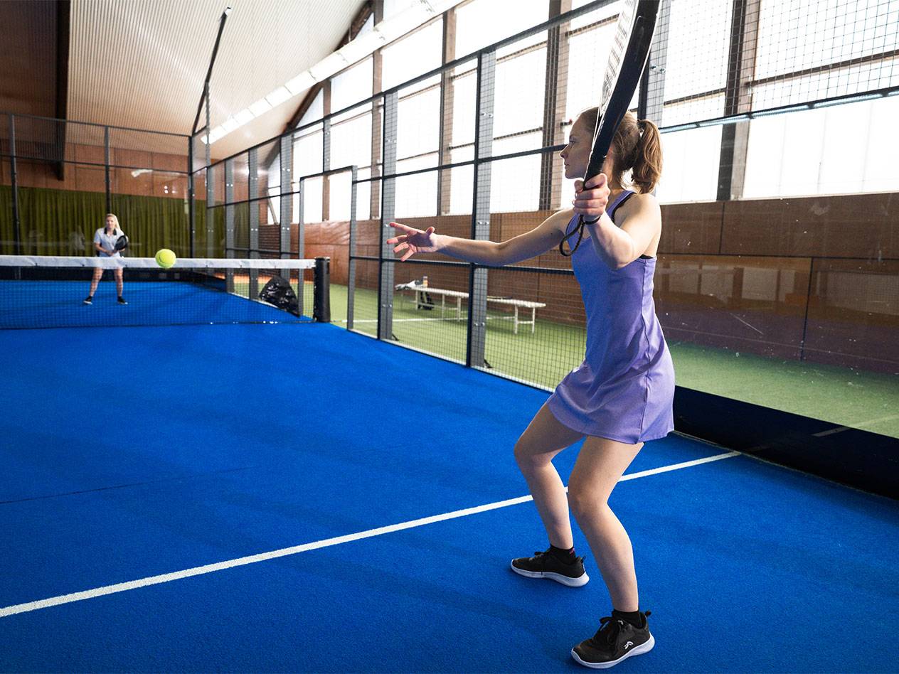 Femme en robe de sport violette jouant au padel sur un court bleu.