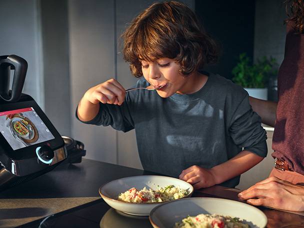 Enfant mangeant dans un bol à côté d'un appareil de cuisine intelligent affichant une recette.