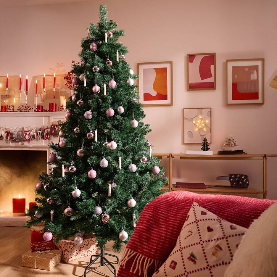Sapin de Noël décoré de boules roses et argentées dans un salon chaleureux.