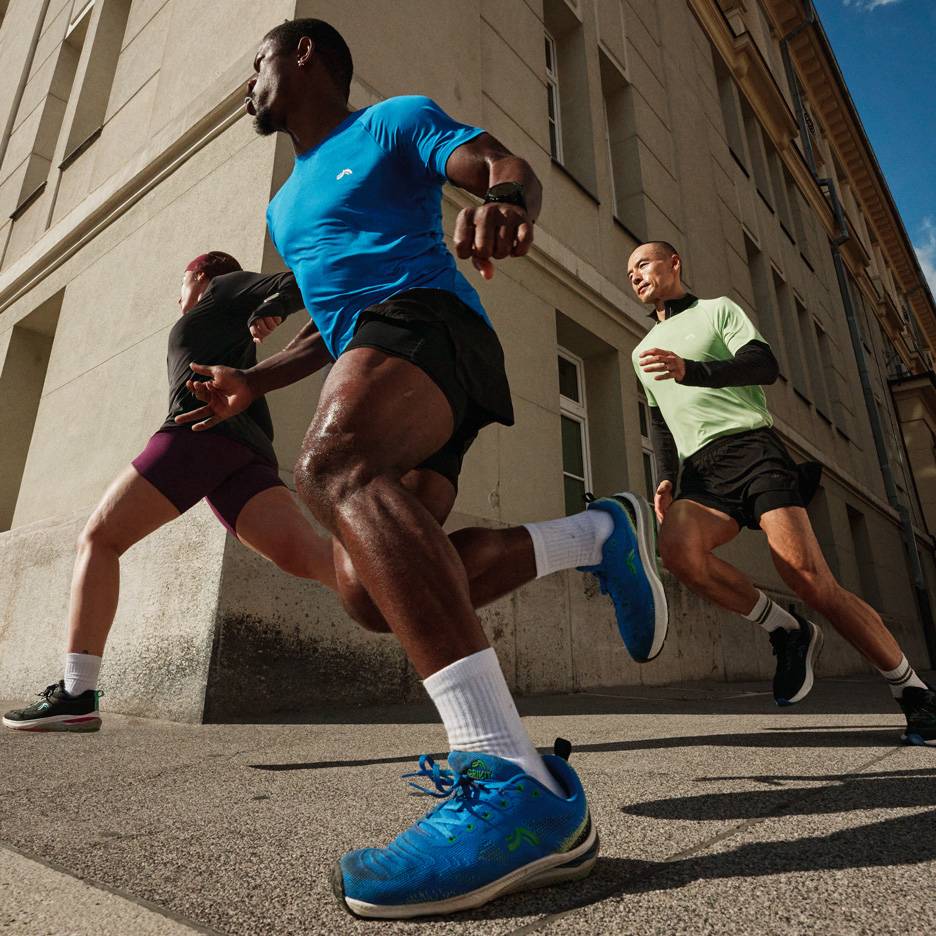 Trois coureurs en t-shirts et shorts de sport courent dans une rue de la ville.