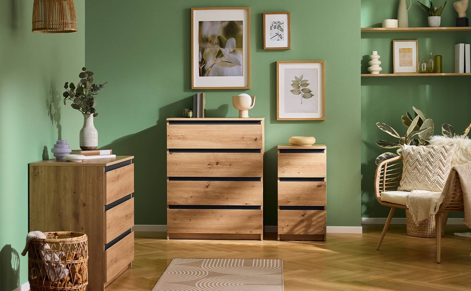 Commode en bois avec tiroirs noirs, décorée de plantes et de cadres sur un mur vert.