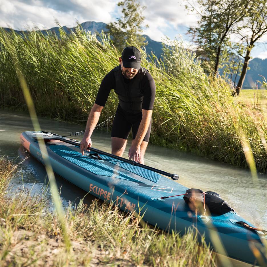 Homme en combinaison noire se préparant à faire du paddle, planche dans l'eau