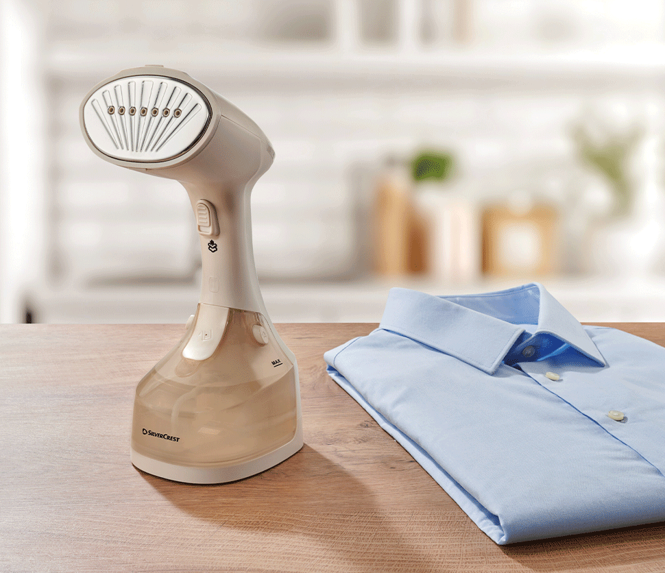 Défroisseur vapeur SilverCrest et chemise bleue pliée sur une table en bois.