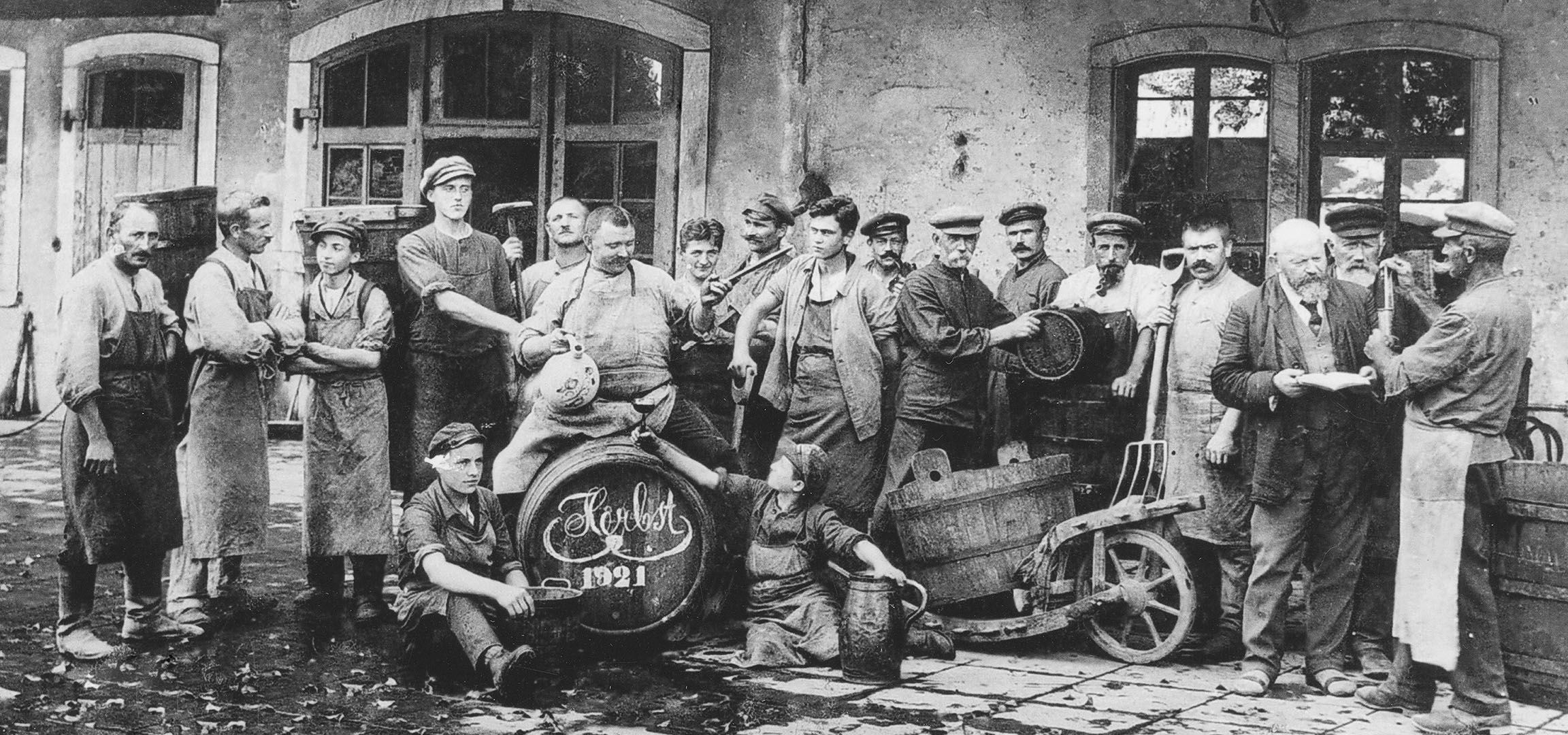 Hommes dans une cave avec des fûts de vin, l'un levant un verre.