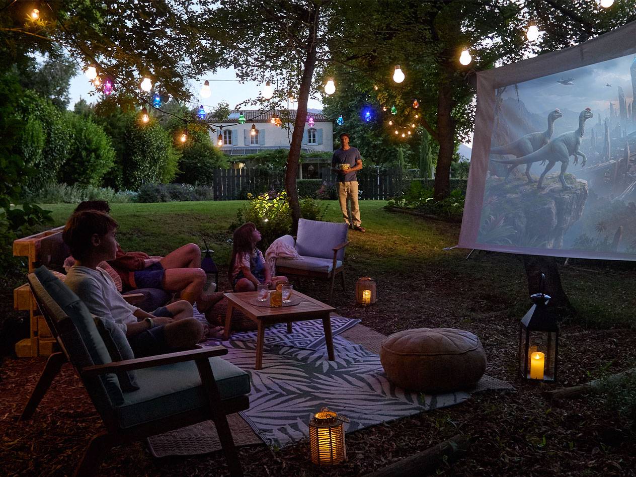 Famille profitant d'une soirée cinéma en plein air avec des guirlandes lumineuses et des meubles de jardin confortables.