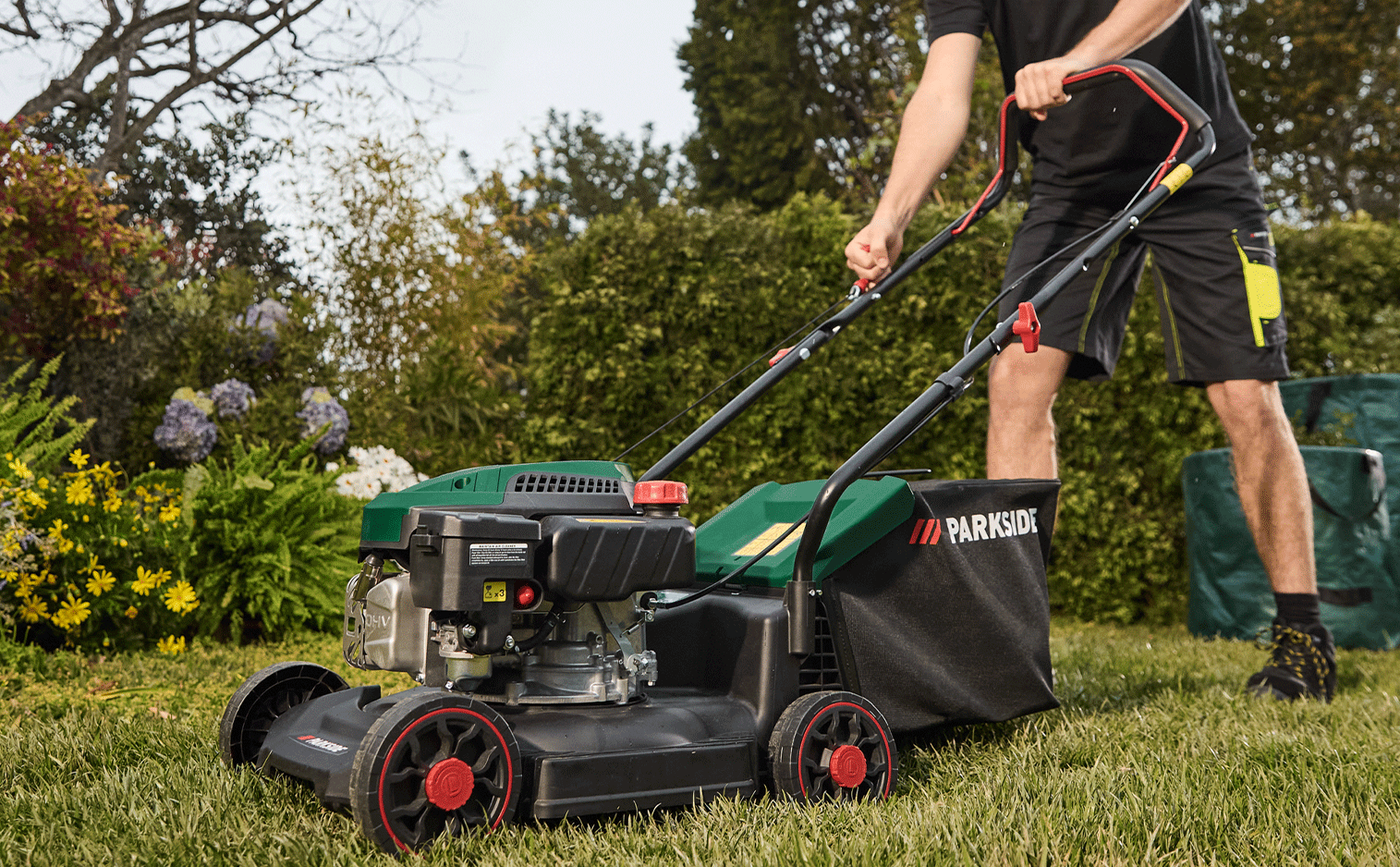 Un homme tond la pelouse avec une tondeuse à gazon dans un jardin fleuri.