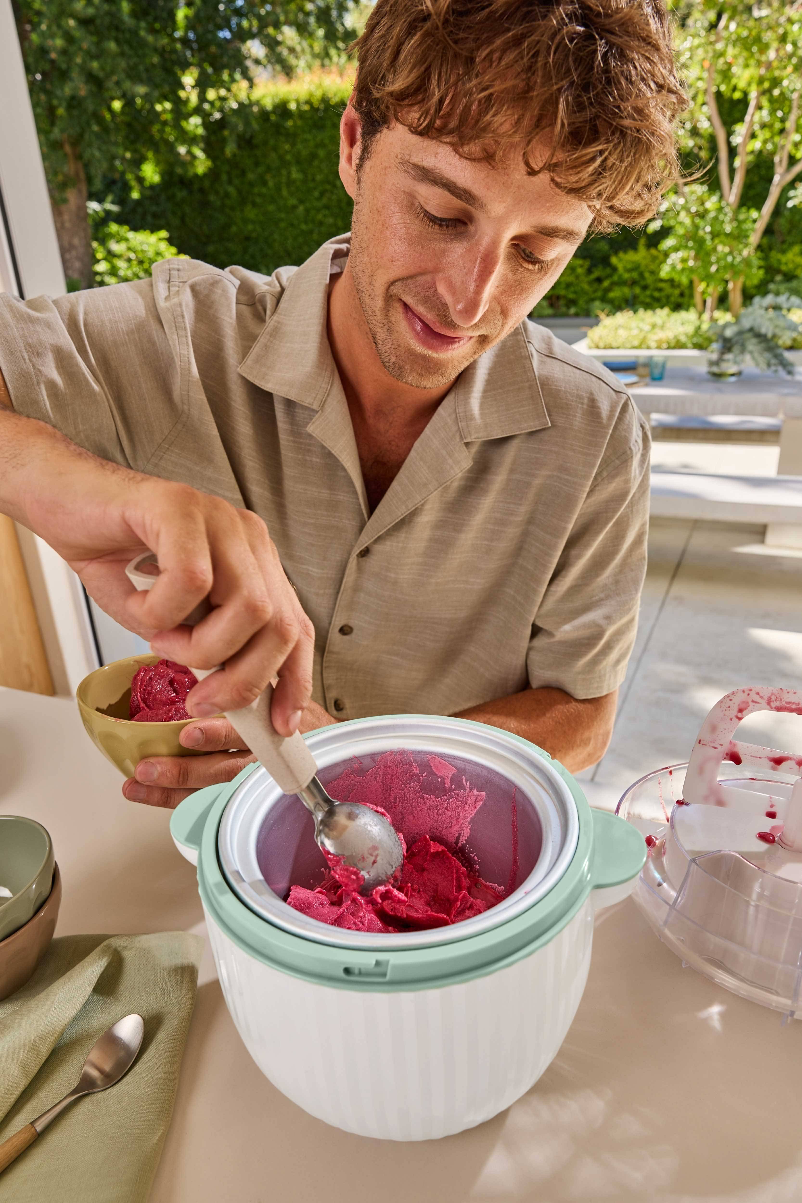 Homme servant du sorbet rouge d'une sorbetière dans un bol.