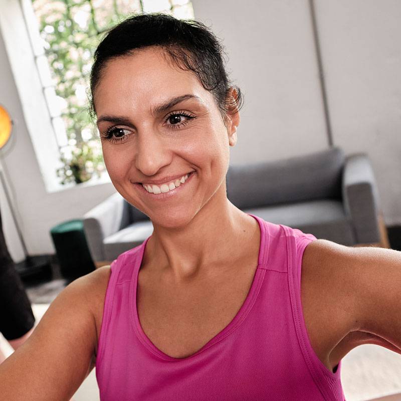 Femme souriante en débardeur rose faisant de l'exercice à la maison.