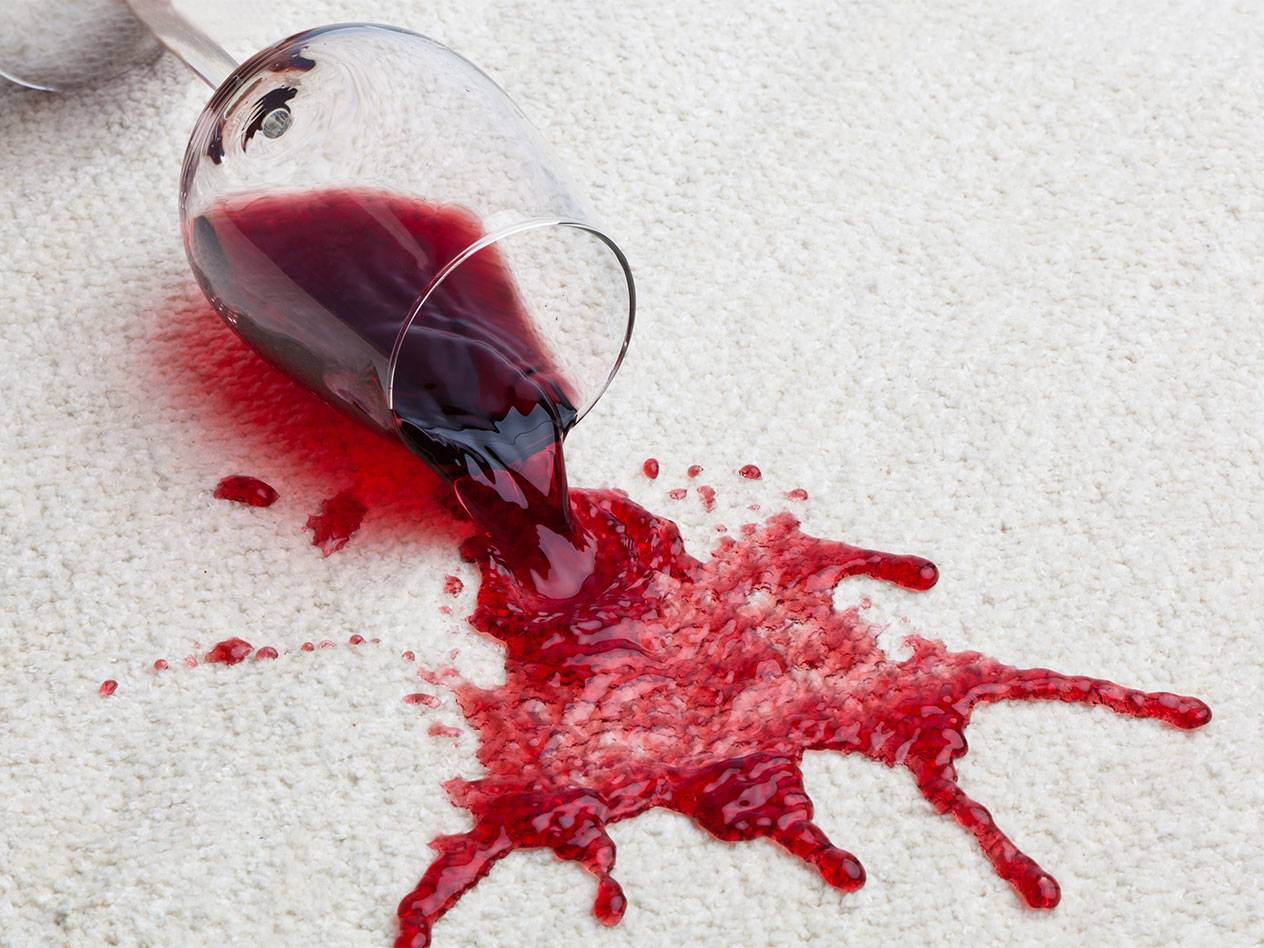 Vin rouge renversé d'un verre sur un tapis blanc