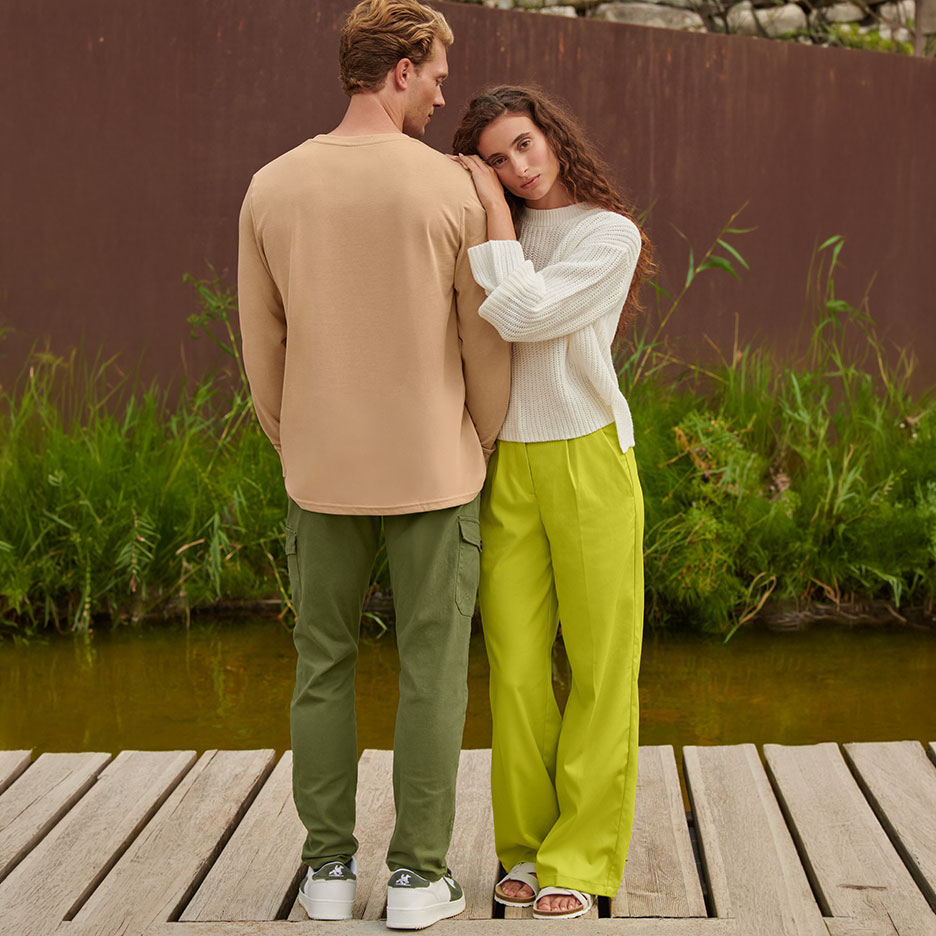 Homme en t-shirt beige à manches longues et pantalon cargo vert, femme en pull blanc et pantalon lime.