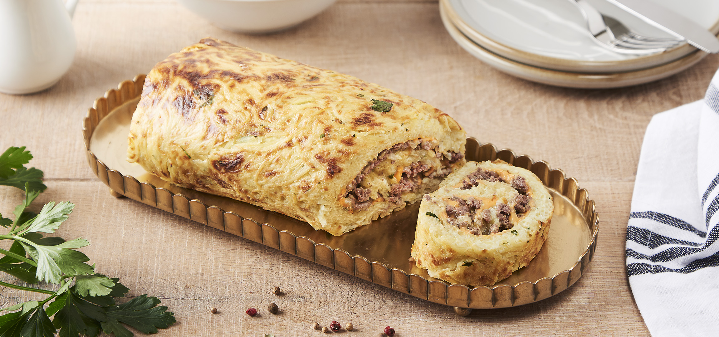 Roulade de pommes de terre farcie à la viande hachée et au fromage, servie sur un plat doré.