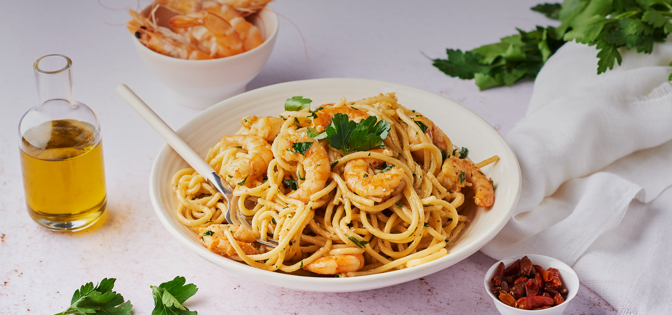 Spaghetti aux crevettes et persil dans un bol blanc avec une fourchette et une bouteille d'huile.