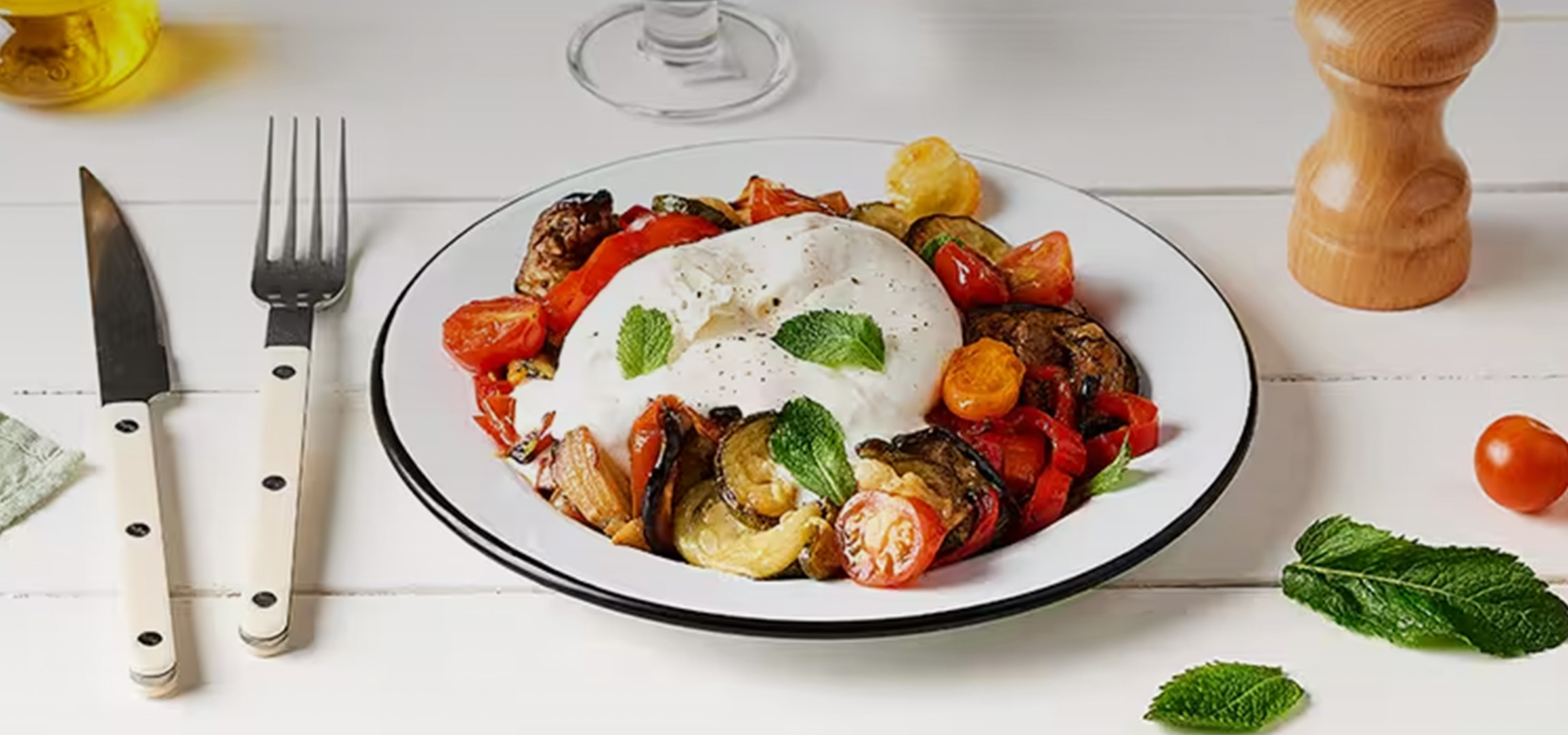 Burrata crémeuse avec légumes grillés colorés et herbes fraîches sur une assiette blanche.